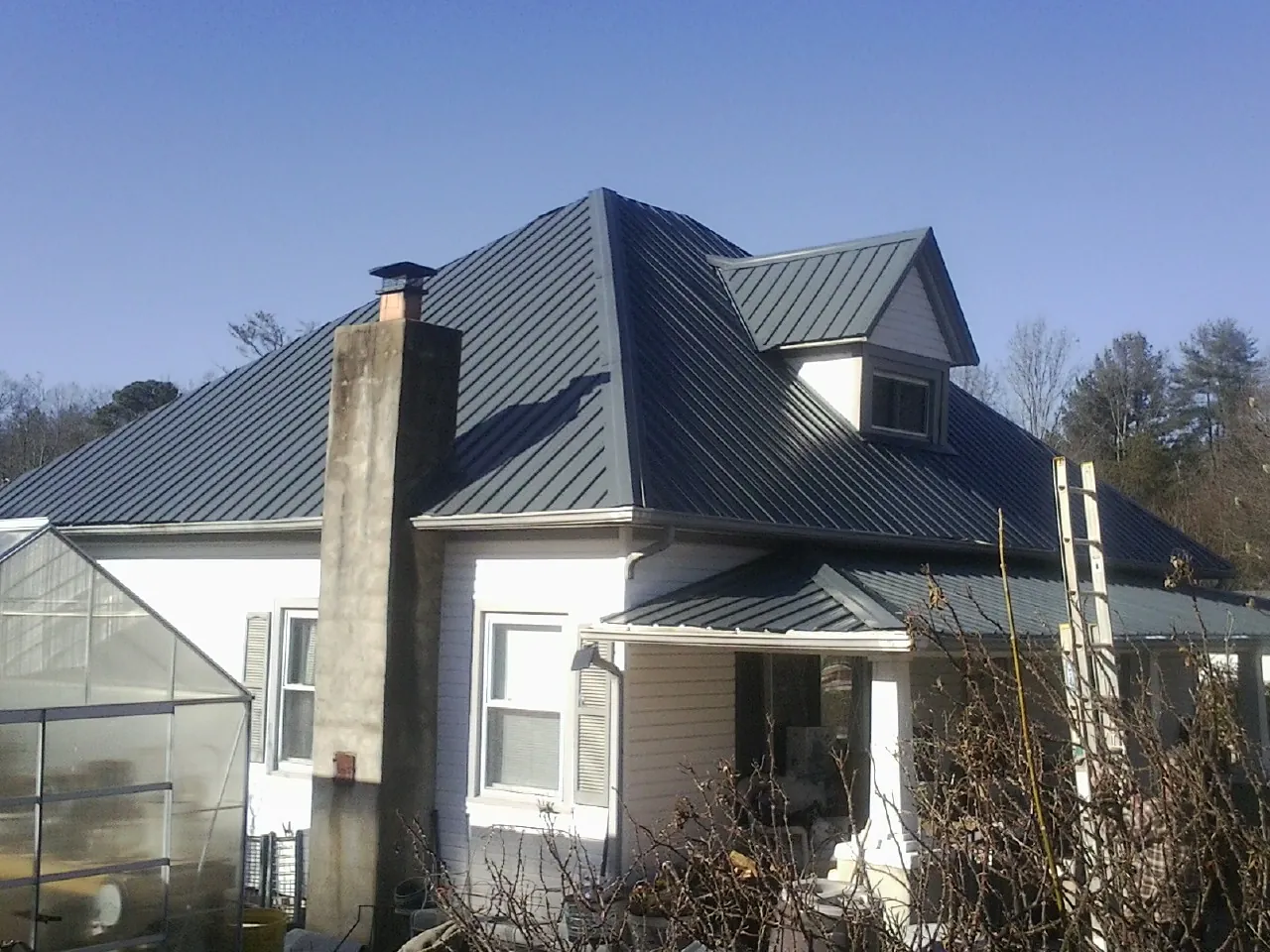 Dark blue standing seam metal roof on a white farmhouse with dormer — Slate & Tile Roof Repair by Roofing Brothers in Valley Cottage