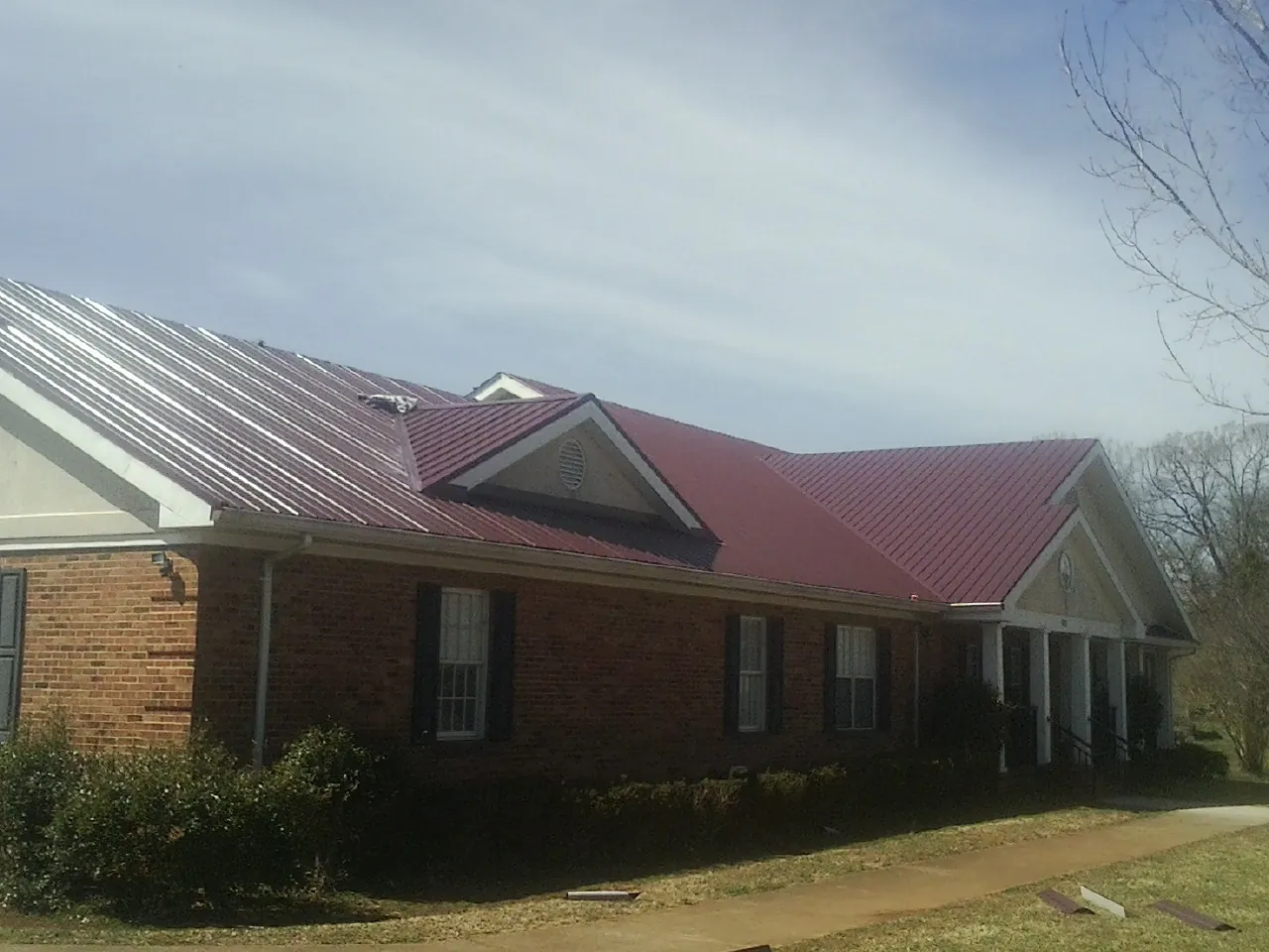 Red metal roof with gabled entries on a long brick building, from a Hail Damage Roof Repair job in Valley Cottage