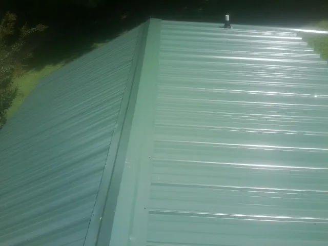 New green metal panels meeting at the ridge of a roof — Flat Roof Repair work by our crew in Valley Cottage
