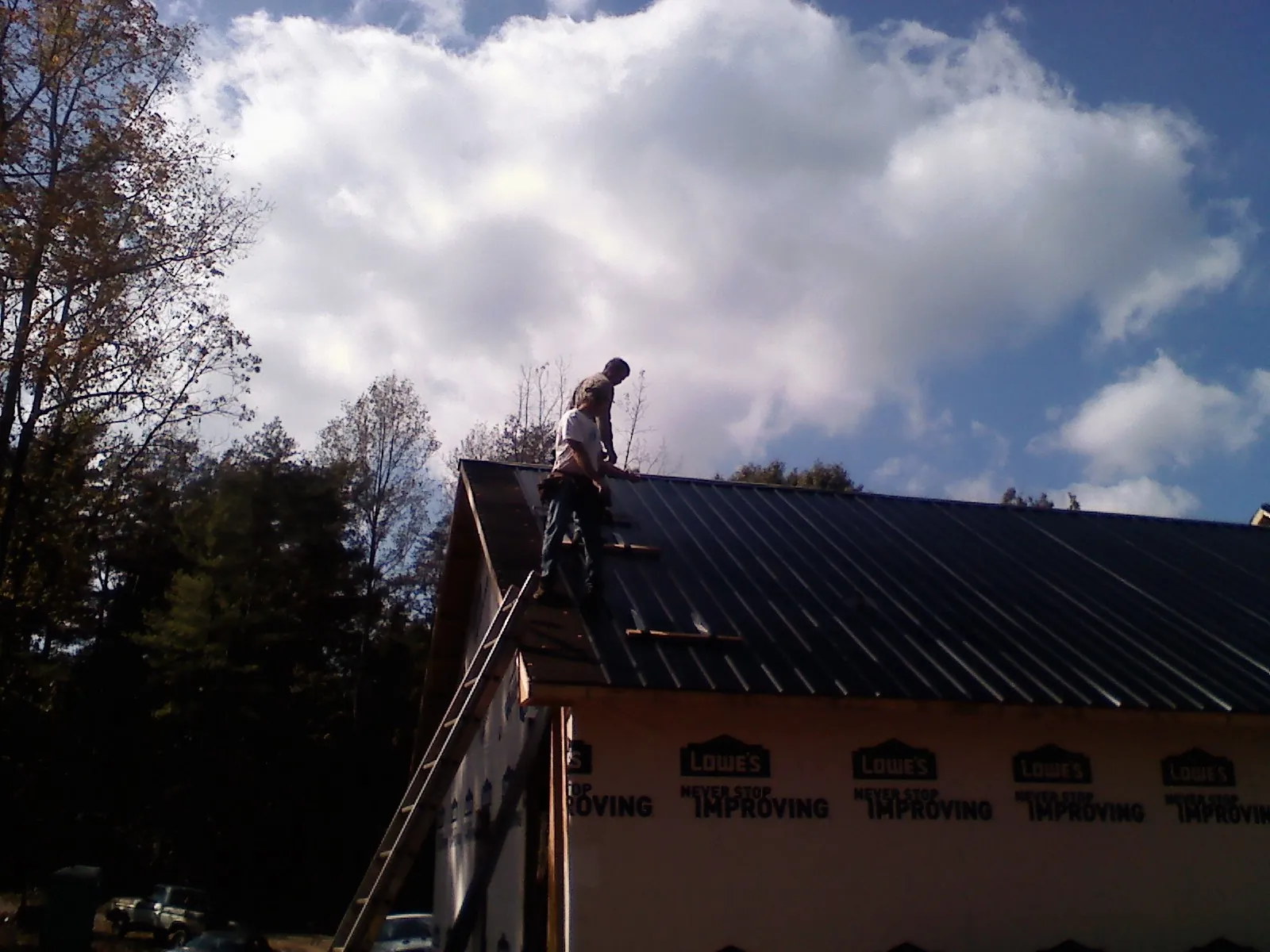 Roofer fastening dark metal panels high against a cloudy sky, from a Roof Inspection job in Valley Cottage