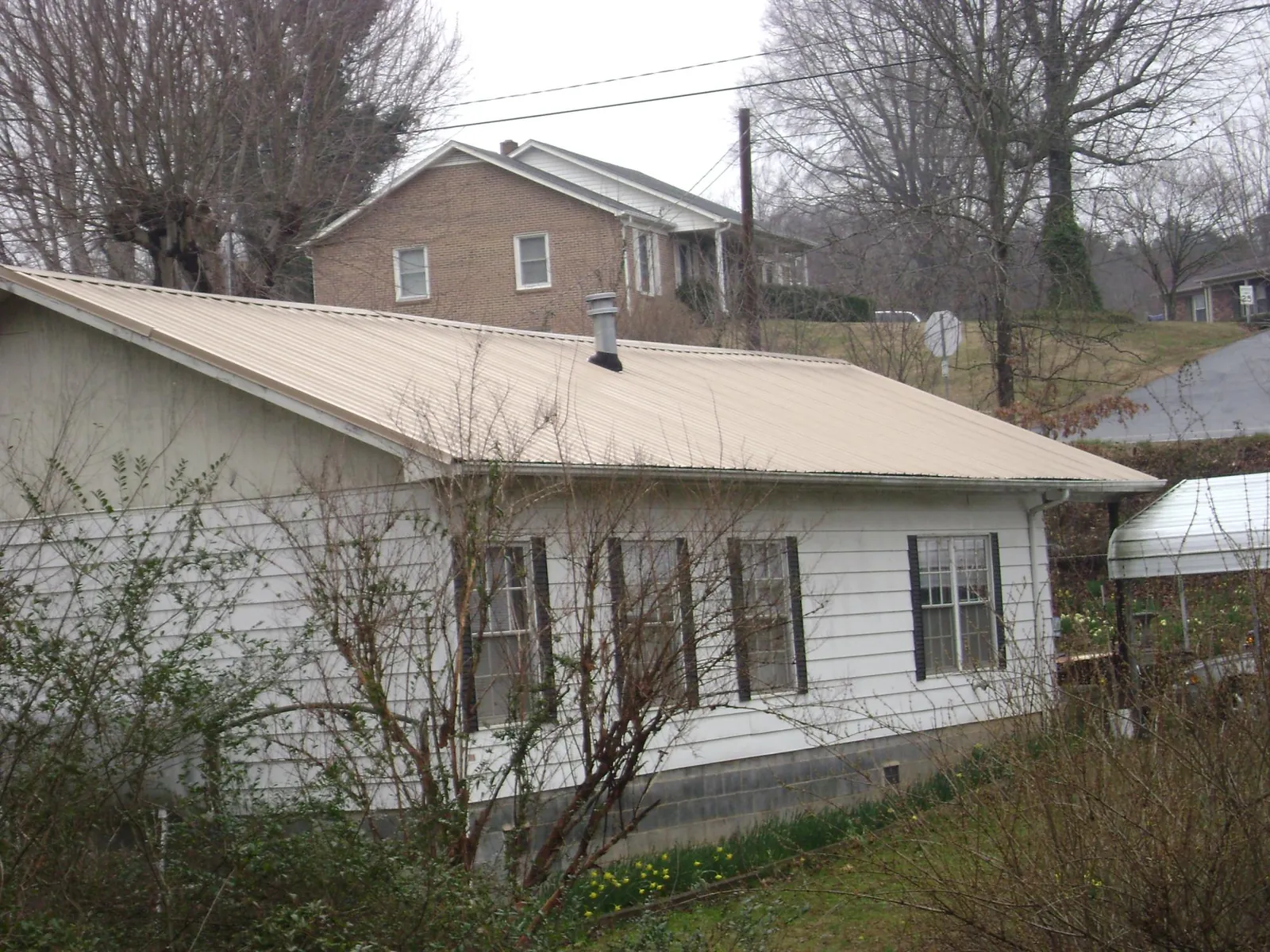 Tan metal roof on a white sided house set into a hillside — Commercial Roofing by Roofing Brothers in Valley Cottage